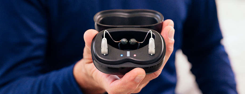 Image of hand holding an open hearing aid charger with hearing aids inside